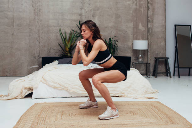 スクワットを練習する若い女性。自宅で運動する女性。 - crouching ストックフォトと画像