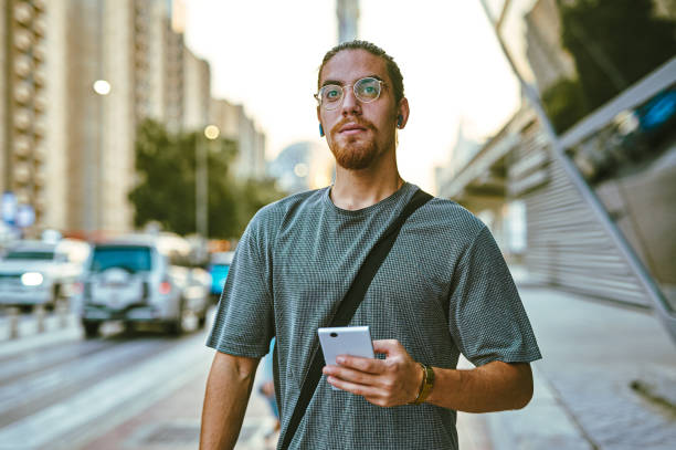 istock Shot of a handsome young man standing alone and looking contemplative while using his cellphone in the city 1370713304