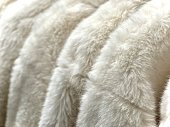 closeup white artificial or faux fur coats hanged in a row in the store