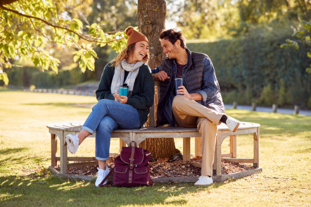 istock Smiling Couple Sitting On Bench In Autumn Park With Reusable Drinks Cups 1370716562