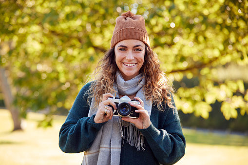 Woman In Autumn Countryside Taking Photo On Retro Style Digital Camera To Post To Social Media