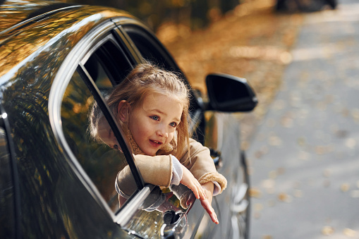 Little girl sitting in the black automobile and looking through the window.