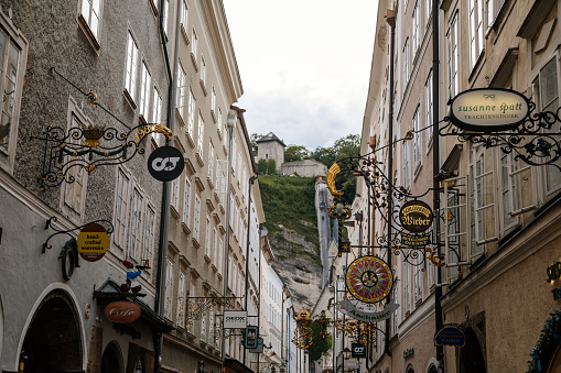 Salzburg, Austria, 28 August 2021: Grain Lane or Getreidegasse famous shopping narrow street in historic Altstadt or Old Town, wrought iron guild signs at summer day, numerous high townhouses skyline
