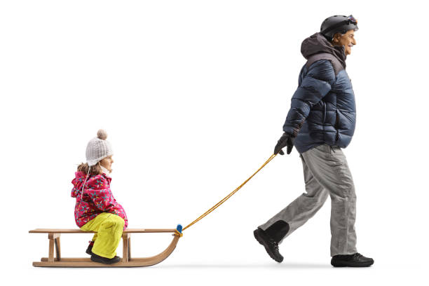 full length profile shot of a mature man in winter clothes walking and pulling a girl on a sled - family winter walking fun imagens e fotografias de stock