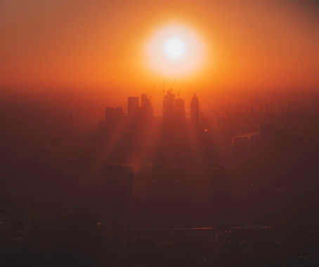 High angle view of early morning silhouetted buildings and sunrise over London City and financial skyscrapers on a misty and foggy day in England, UK. Environmental pollution concept of cityscape in smoke.
