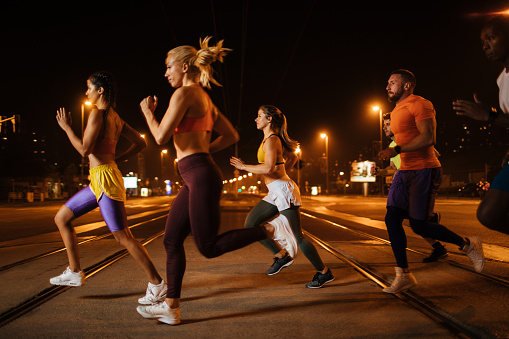 Team of athletic young people running through the city streets at night