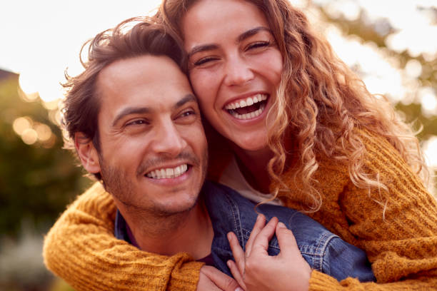 retrato de una feliz pareja amorosa con un hombre que le da piggyback a la mujer mientras se abrazan juntos en autumn park - couple fotografías e imágenes de stock