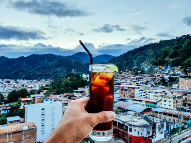 Hand of a man with a drink with the view of the city of Chanchamayo located in the department of Junin in Peru. Hand of a man with a drink with the view of the city of Chanchamayo located in the department of Junin in Peru cuba libre stock pictures, royalty-free photos & images