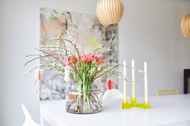A modern Easter bouquet with tulips and twigs stands in a bright environment on a white table in a glass vase
