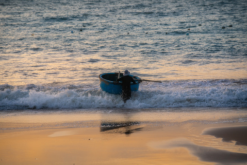 A fisherman is putting the basket boat against the waves on Phan Thiet beach, Binh Thuan province, central Vietnam