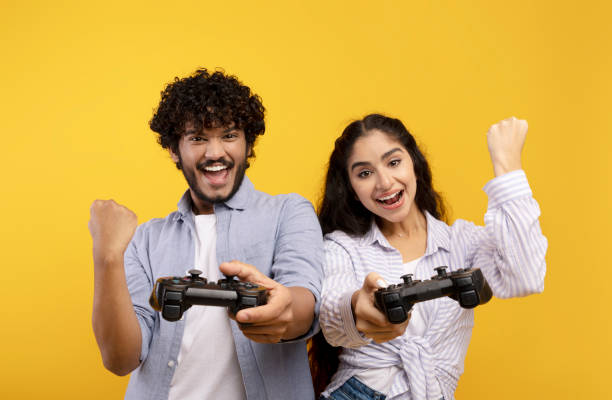 concepto de entretenimiento de tiempo libre. pareja india juguetona jugando videojuegos juntos, sosteniendo y usando joysticks - shaking fist fotografías e imágenes de stock