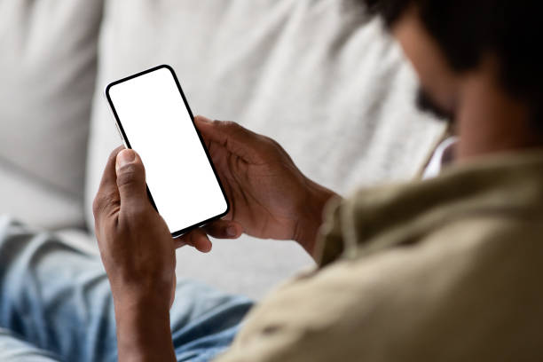 maschio nero irriconoscibile che utilizza lo smartphone con schermo bianco vuoto a casa - folto foto e immagini stock