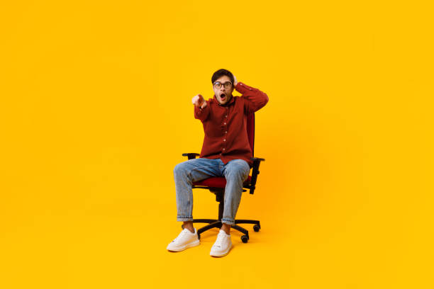 istock Shocked Man Pointing Finger At Camera Sitting Over Yellow Background 1370730169