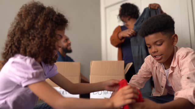 Parents with children sorting out clothes in boxes to donate at home