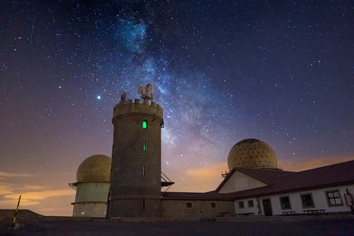 Astrophotography image of the stars and nebula of the Milky Way galaxy in the night sky. This was taken in front of the observatory and tower on top of the Serra da Estrela mountain range in the natural park in Portugal.