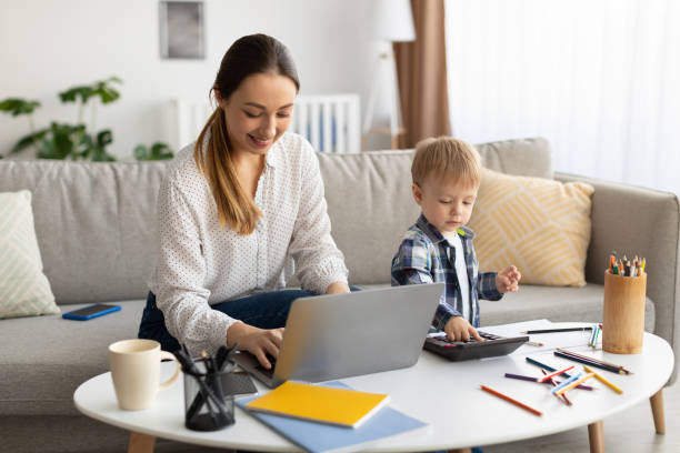 istock Freelancing at maternity leave. Young mother working on laptop while her toddler son playing with calculator neaby 1370731421