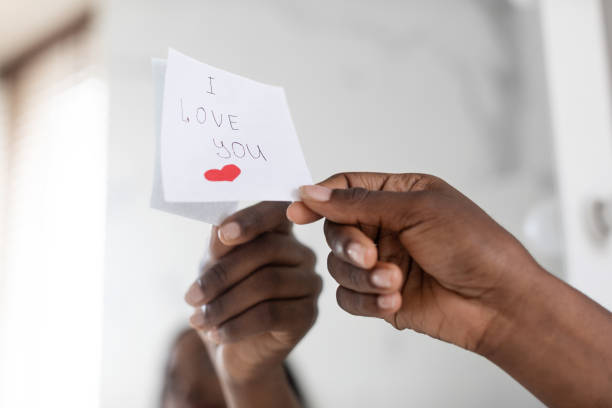 Black Female Hand Putting Sticky Note With Love Message On Mirror, Closeup Black Female Hand Putting Sticky Note With Love Message On Mirror, Closeup Shot Of Unrecognizable African American Woman Sticking Paper With I Love You Text And Drawn Heart, Cropped Image mirror writing stock pictures, royalty-free photos & images