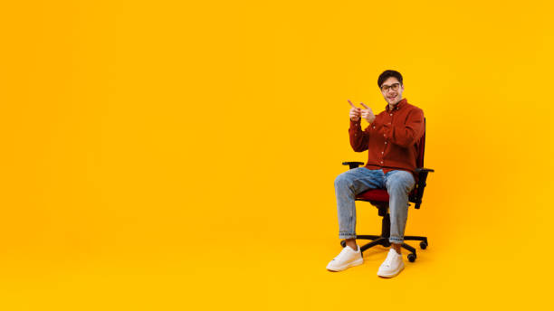 istock Man Pointing Fingers Aside Showing Free Space Sitting, Yellow Background 1370731452