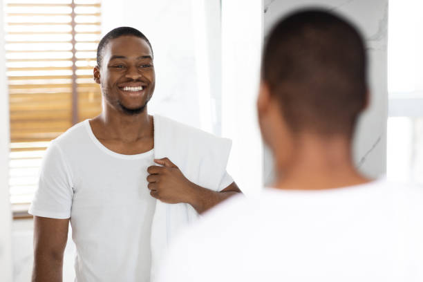 istock Black Handsome Man With Towel On Shoulder Looking At Mirror In Bathroom 1370731712