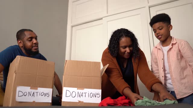 Parents with son sorting out clothes in boxes to donate at home