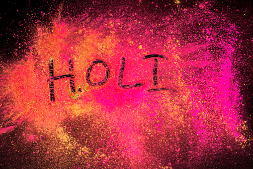A black wood board full of holi festival powder colors and Holi written by Finger on it. Concept of Holi festival.