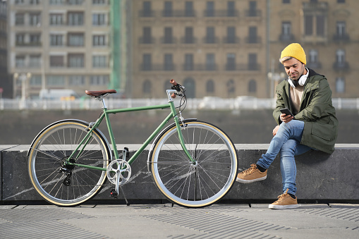 Hispanic man using phone beside classic bicycle in the city