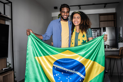 Portrait of a happy young couple holding brazilian flag at home