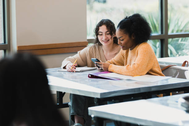 Teen girls take break to mess with phone Two teenage girls take a break from their schoolwork to play with a smart phone. teenagers only teenager multi ethnic group student stock pictures, royalty-free photos & images