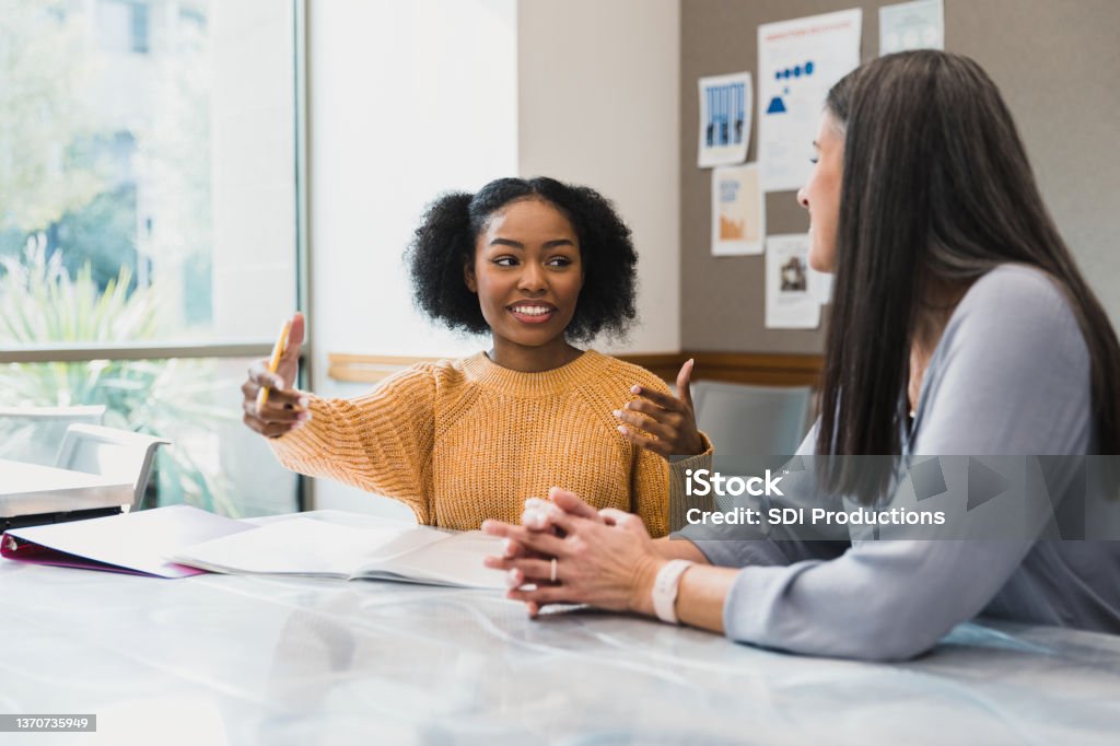 Teen girl gestures while explaining something to female teacher The teenage girl gestures as she explains something to her mid adult female teacher. Student Stock Photo