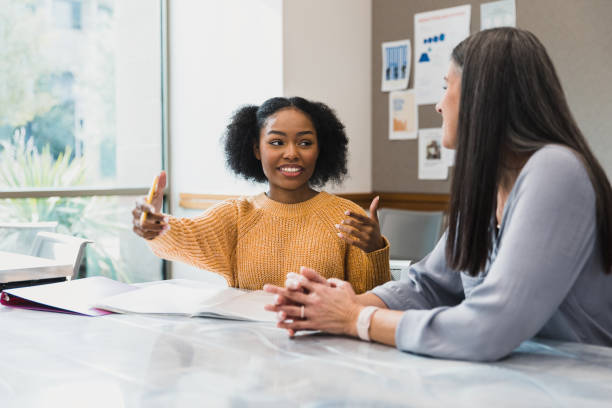 Teen girl gestures while explaining something to female teacher The teenage girl gestures as she explains something to her mid adult female teacher. teaching stock pictures, royalty-free photos & images