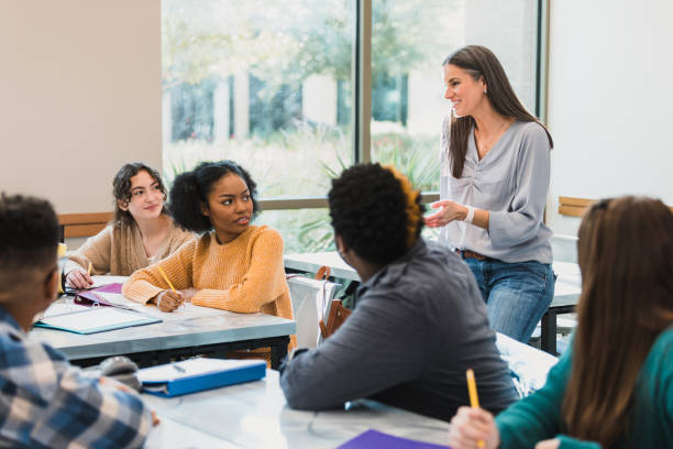 Relaxed female teacher talks to teen students In a relaxed moment during the school day, the mid adult teacher talks to her multi-ethnic teenage class. high school teacher stock pictures, royalty-free photos & images