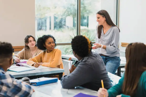 Photo of Relaxed female teacher talks to teen students