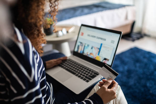 mujer joven comprando en línea usando la computadora portátil en casa - ecommerce fotografías e imágenes de stock