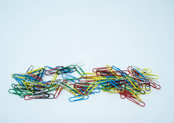 Multi coloured, blue, red, yellow, black and green paper clips in a pile on a plain white background.