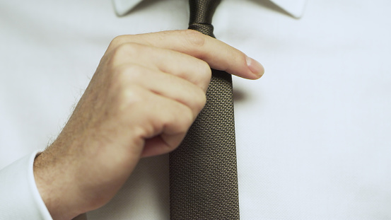 The man straightens his brown tie.