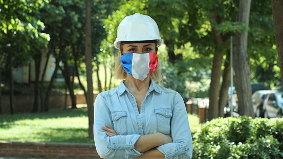 Portrait of female engineer with medical mask with France flag and white helmet.