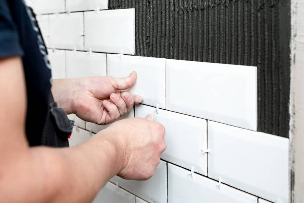 istock The master's hands press a white ceramic tile against the wall The stage of facing the kitchen wall with white ceramic tiles. Construction details, repair work 1370741223