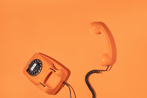 Old phone on bright bold orange background. Retro aesthetic style. Trendy minimal flat lay. Spring or summer sunny idea. Colorful telephone handset concept.
