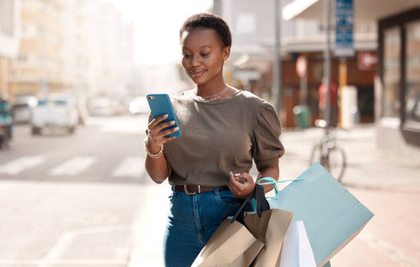 街で買い物をしている間、外で彼女の携帯電話を使用して魅力的な若い女性のショット - ショッピング ストックフォトと画像