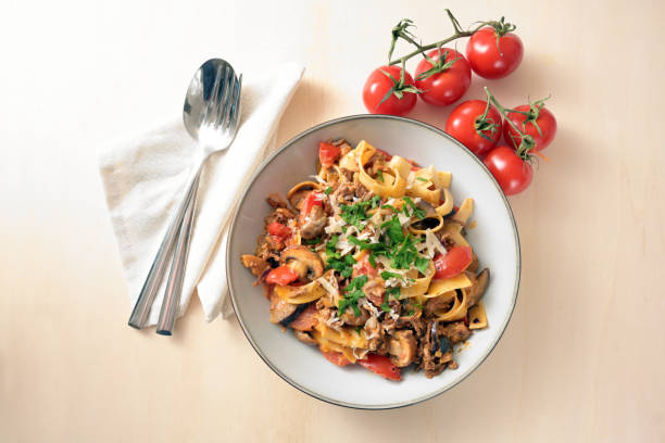 タンキ肉、トマト、野菜のソースを持つタリアテッレ、パルメザンチーズとパセリのテーブル、薄い木製テーブル、コピースペース、上からの高角度ビュー、選択されたフォーカス - dishware pasta tagliatelle beef ストックフォトと画像
