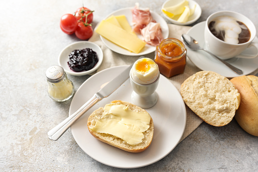 Breakfast with rolls, egg, jam, cheese and ham and a cup of coffee, light rustic background with copy space, selected focus, narrow depth of field