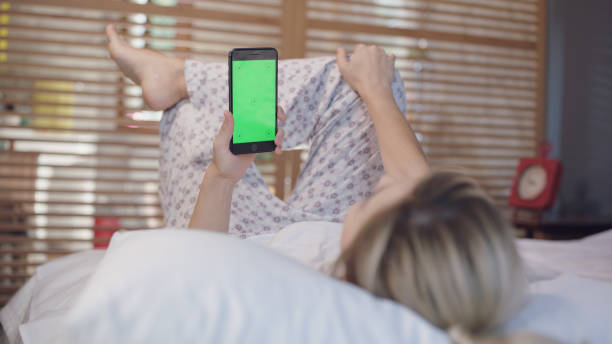 istock Young woman with cell phone on bed, shoulder view. 1370745931
