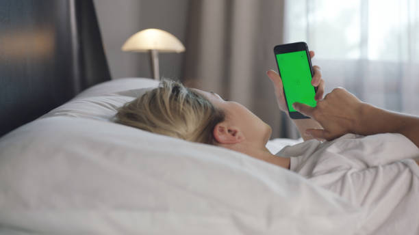 istock Young woman with cell phone on bed, shoulder view. 1370747171
