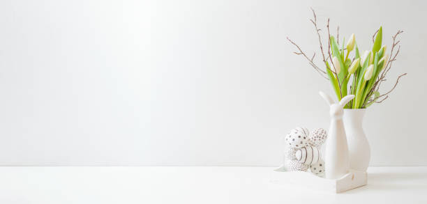istock White spring tulips in a vase, easter eggs on a white table. Mock up for displaying works 1370748352