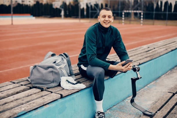 istock Happy athlete with a prosthetic leg using smart phone and wireless earphones while relaxing at the stadium 1370749675