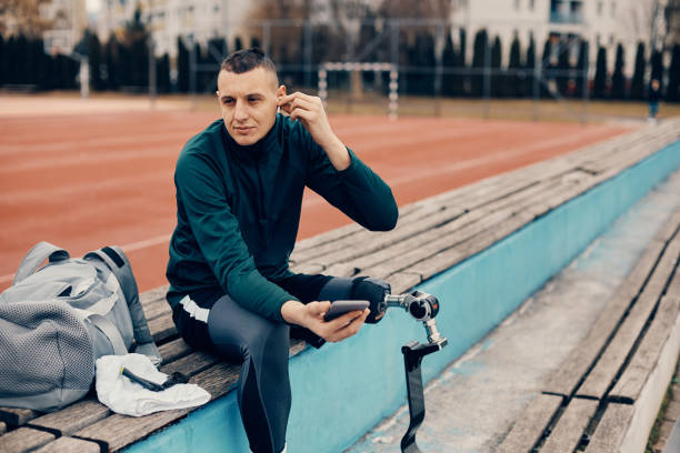 istock Athletic man using smart phone and wireless earphones while relaxing at the stadium after the practice. 1370749677