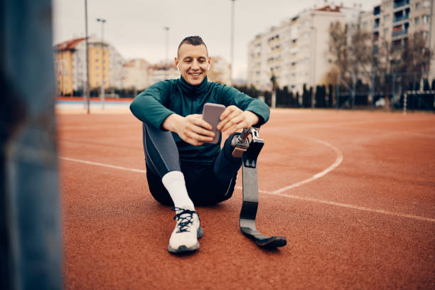istock Happy athlete with a leg disability using smart phone while relaxing after sports training outdoors. 1370749918