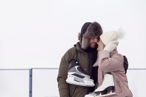 Kissing Loving  Caucasian Couple On Skatingrink With Ice Skates Posing Together Embraced Over a Snowy Winter Landscape. Horizontal Image Composition