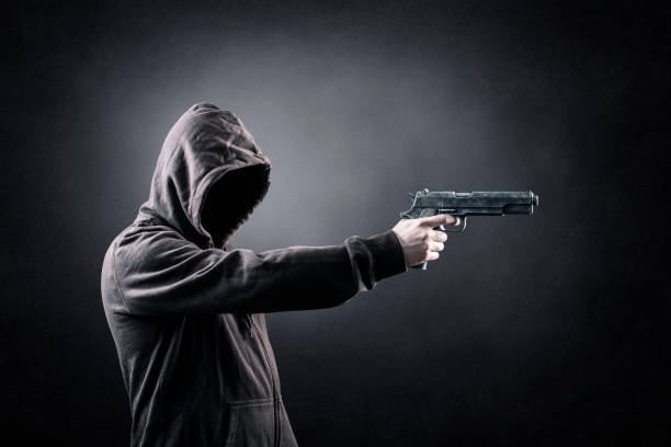 istock Hooded man with a gun in the dark 1370751640