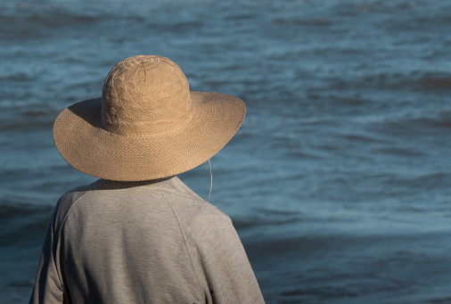close up of an older lady in a hat looking out to sea on a sunny afternoon. The lady is on her back and she is wearing a gray sweatshirt.